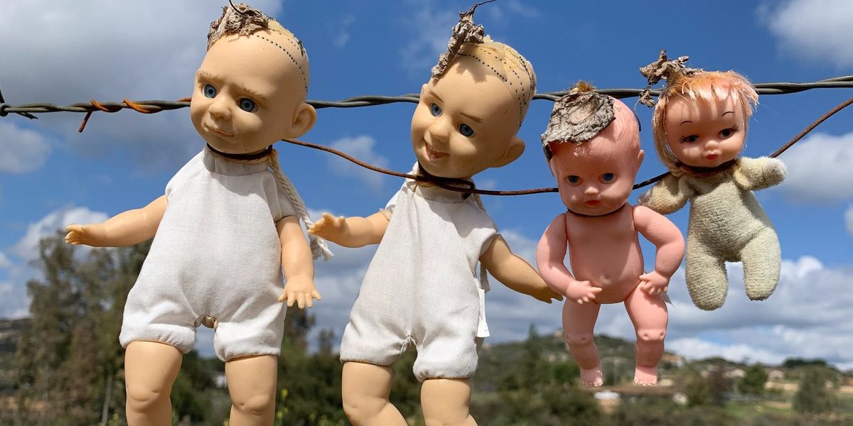 Four small baby dolls hang from a barb wire fence
