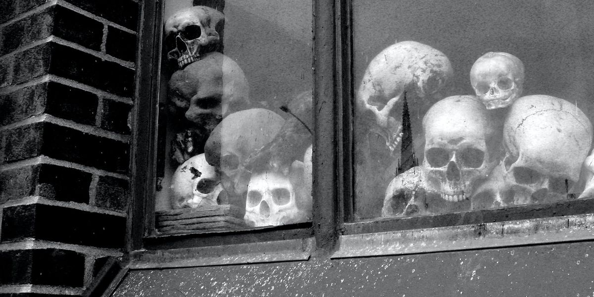 A black and white photo of a window, on the inside there are a pile of skulls