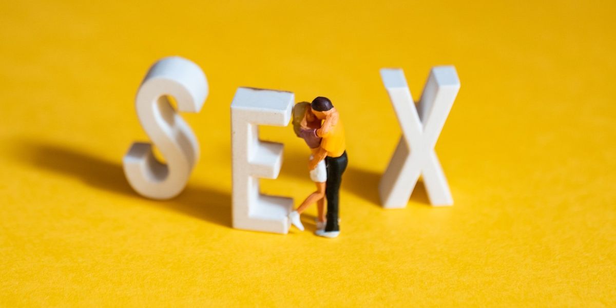 Clay people kiss on a yellow floor, against the letter E in a clay version of the word SEX