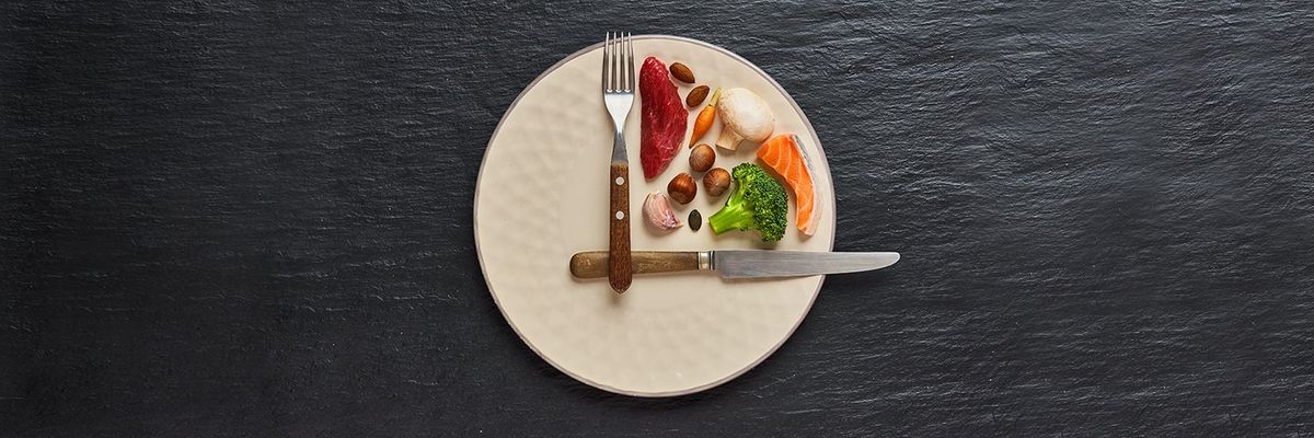 a plate has a fork and a knife set at the 12 and 3 position to mimic clock hands with food inbetween the utensils