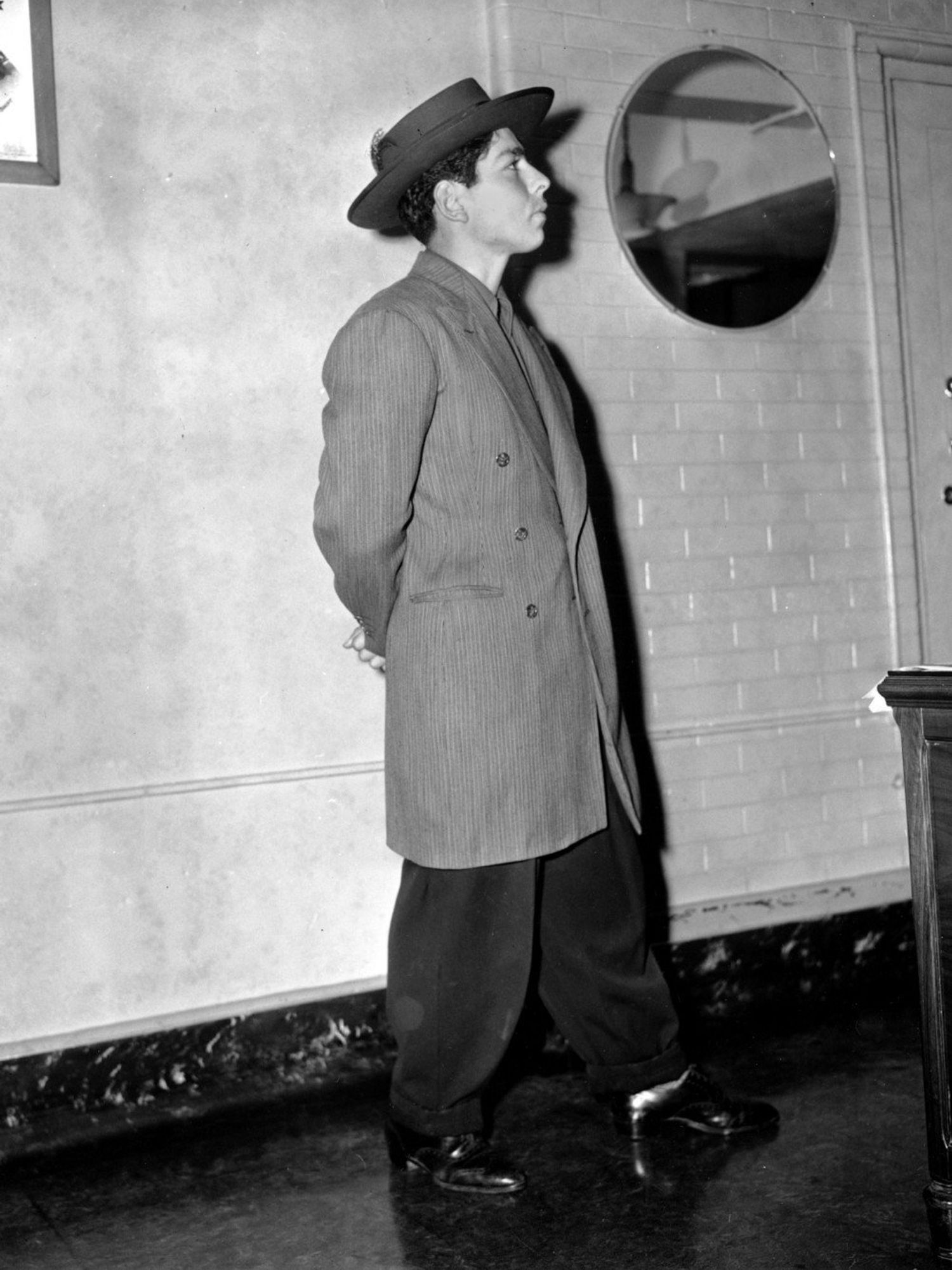 Black and white photo of a man in a zoot suit and pancake hat in a Los Angeles County jail during the Zoot Suit Riots in 1943.