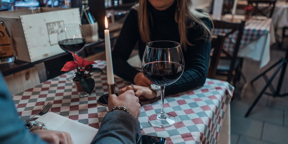 A couple holds hands on a date, candlelit table and two glasses of red wine