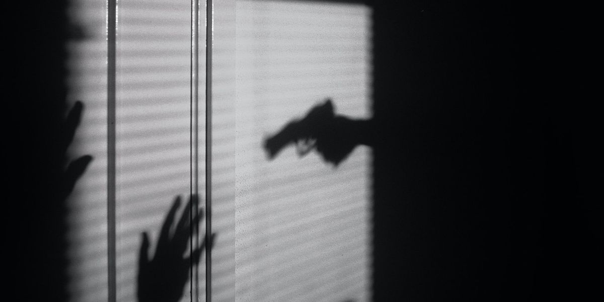 A black and white photo, of the shadow of a gun barring down on someone surrendering