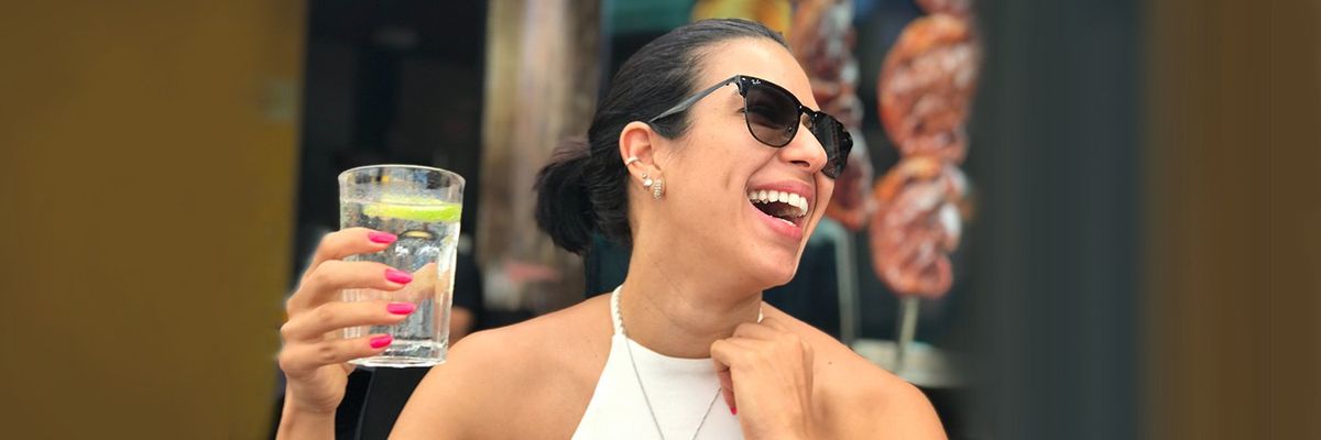 a woman with sunglasses laughing while holding a glass of water with a lemon wedge in it