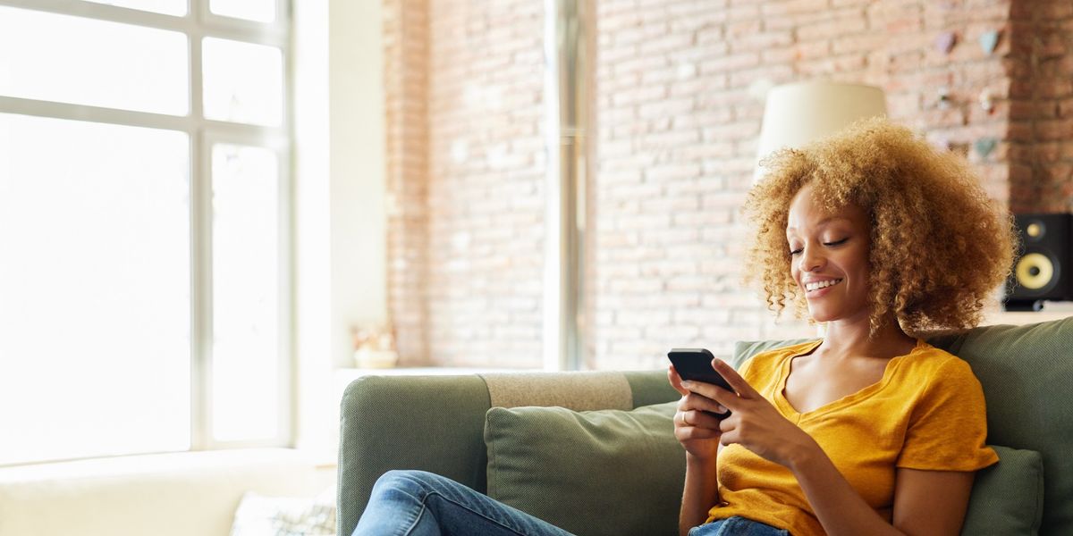 young-woman-with-curly-hair-smiling-at-her-phone-sitting-on-the-couch-at-home