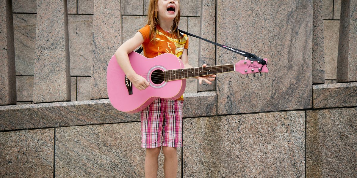 girl busker playing guitar and singing in front of wall