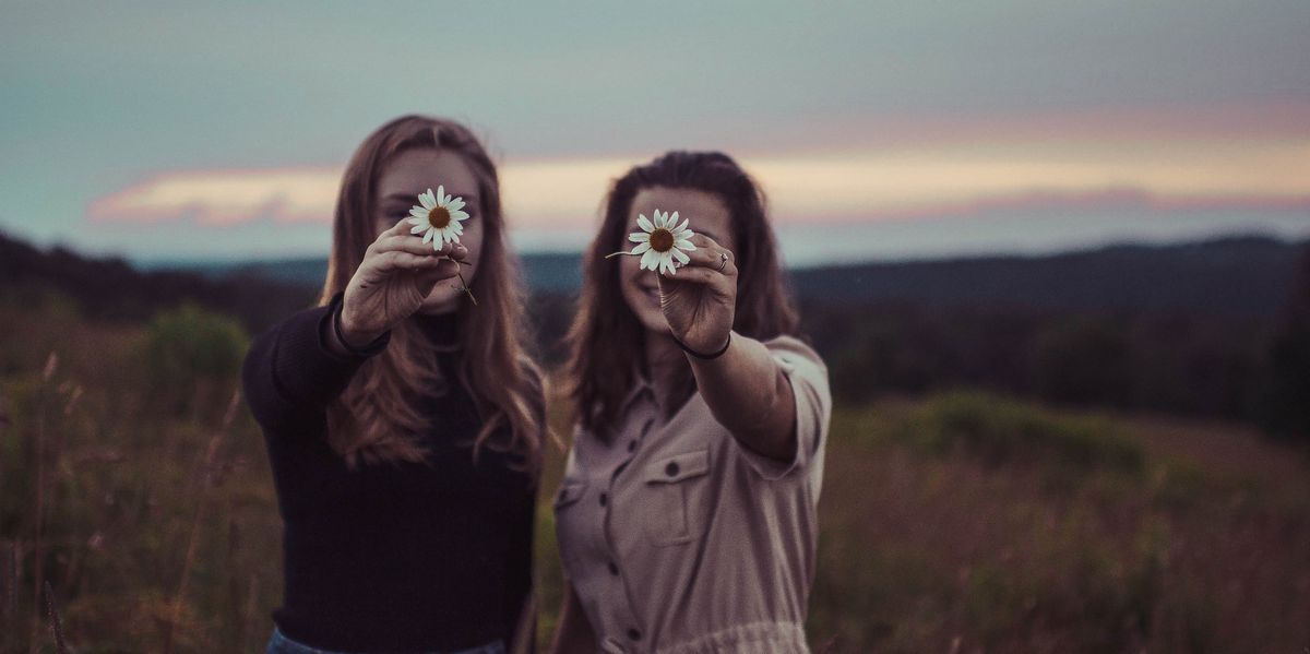 Two women holding up daisies 