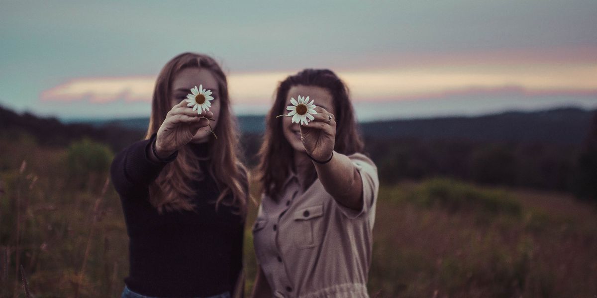 Two women holding up daisies