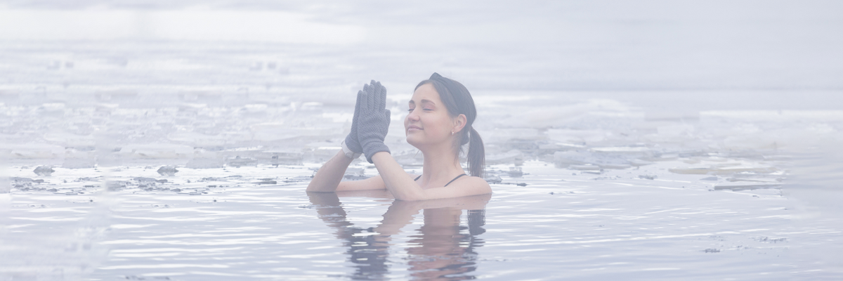 A woman in a frozen lake with her hands together and her eyes closed