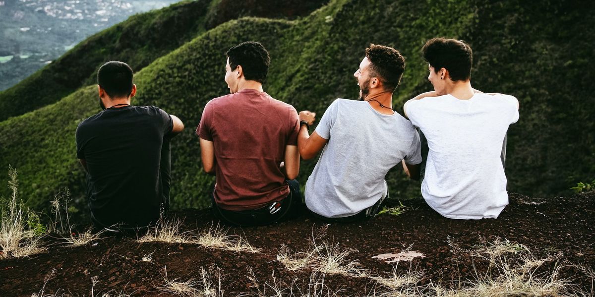Four young men laugh and talk on a hillside
