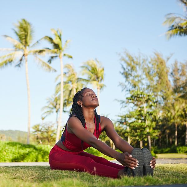 Happy-woman-sitting-on-ground-legs-straight-and-together-holding-her-feet-in-a-stretch