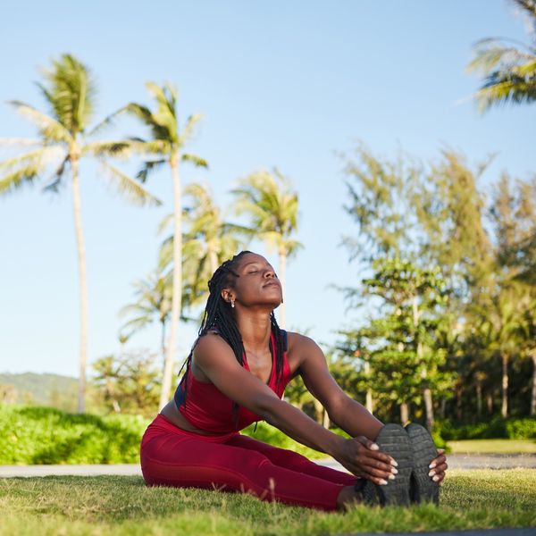 Happy-woman-sitting-on-ground-legs-straight-and-together-holding-her-feet-in-a-stretch