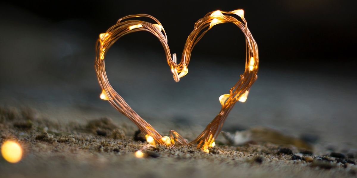 Picture of a heart constructed  of wire and white lights and it sits on sand