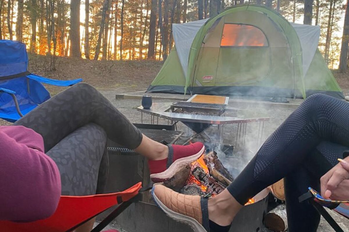 two women sit around a campfire wearing sneakers and leggings