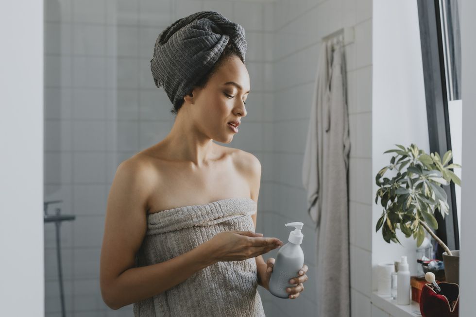 Woman Wrapped in a Towel after a Shower Holding a Skin Care Product