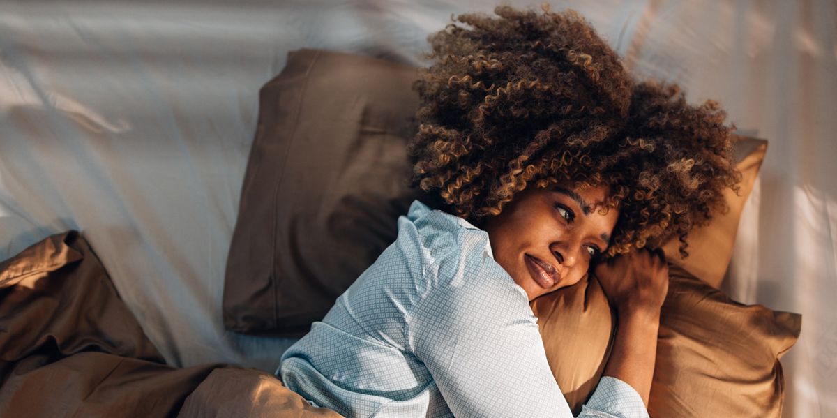 A From Above View Of A Happy Beautiful Woman In Pajamas Looking Away While Lying In Bed