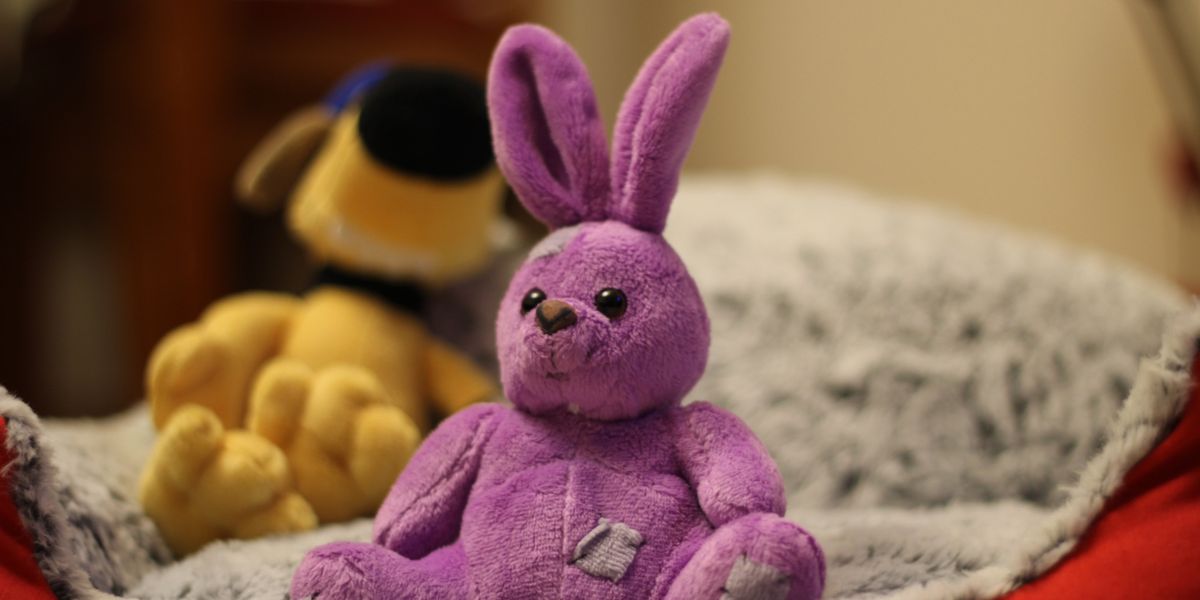 Old, pink stuffed animal bunny sitting on bed
