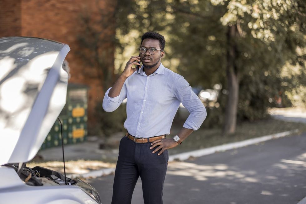 a man standing next to a car that broke down and he is on his cellphone