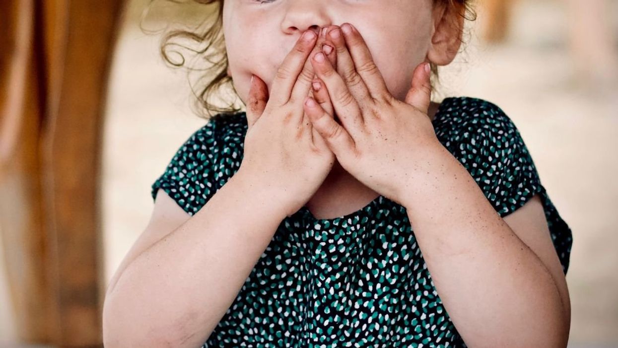 Little girl covering her mouth with both hands
