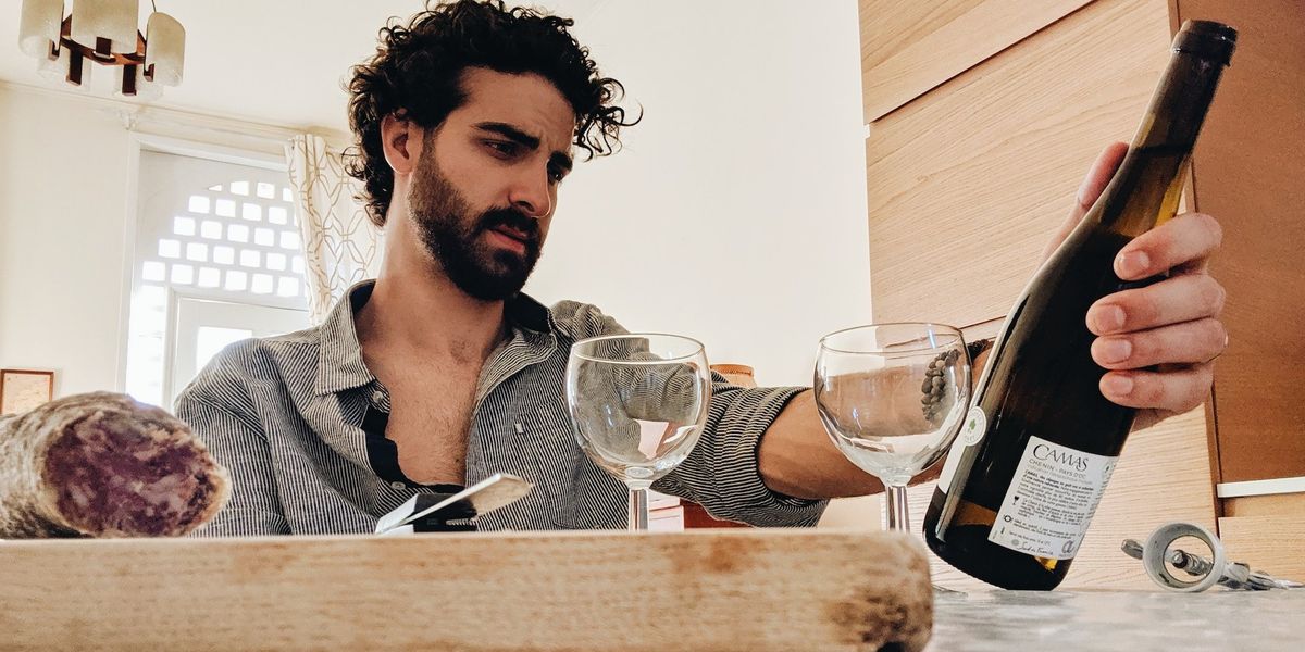 A stressed out guy looks at a bottle of wine and eats in a fancy kitchen