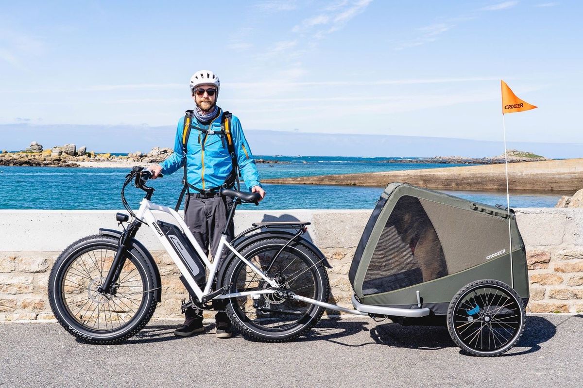 a man with an ebike pulling a dog in a carrying trailer