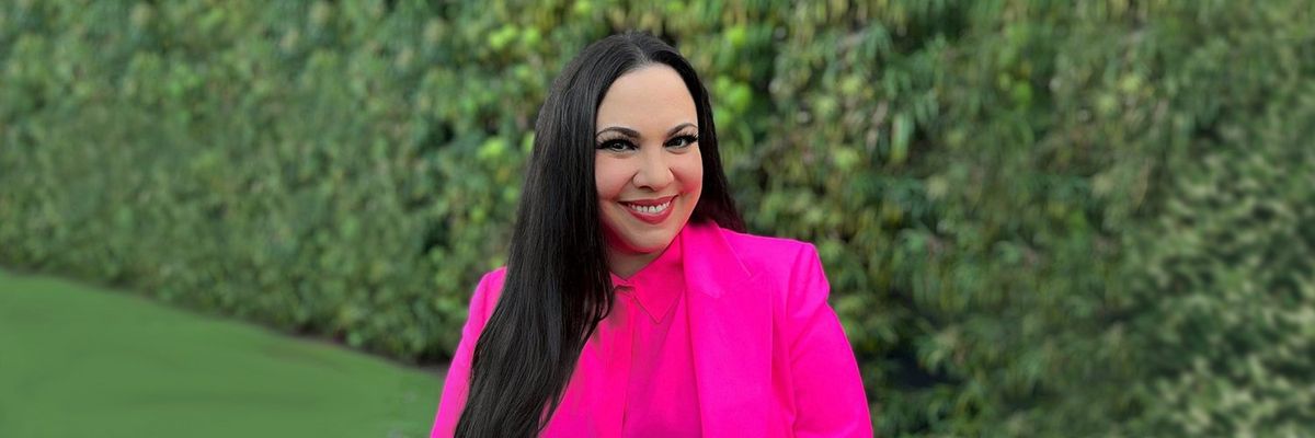 Photo of Gloria Calderón Kellet in a pink blazer and blouse with a green background