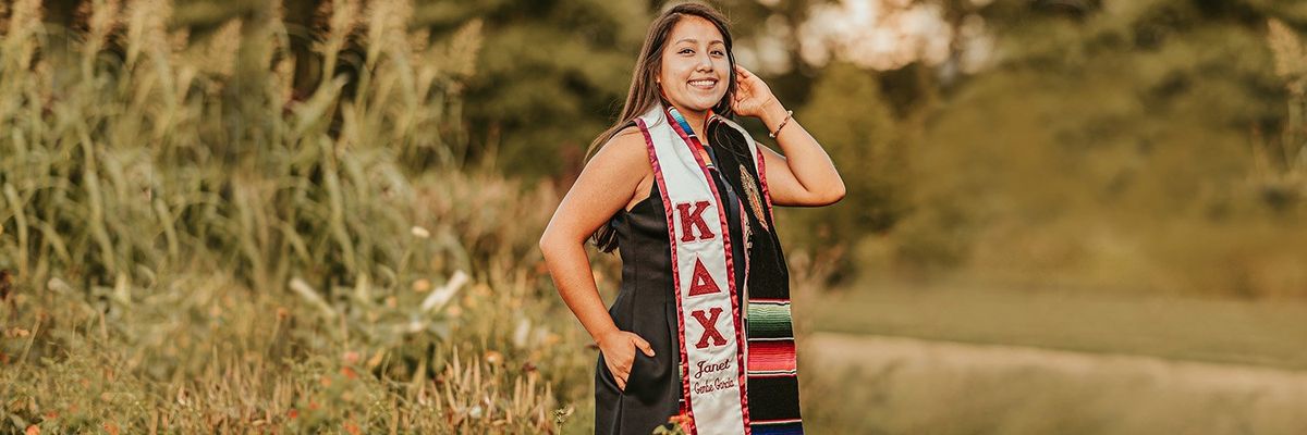 A girl in her greek life academic regalia standing in a field