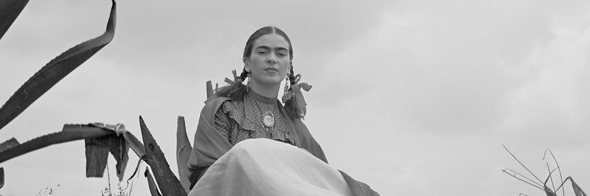 a black and white photograph of Frida Kahlo sitting next to an agave plant