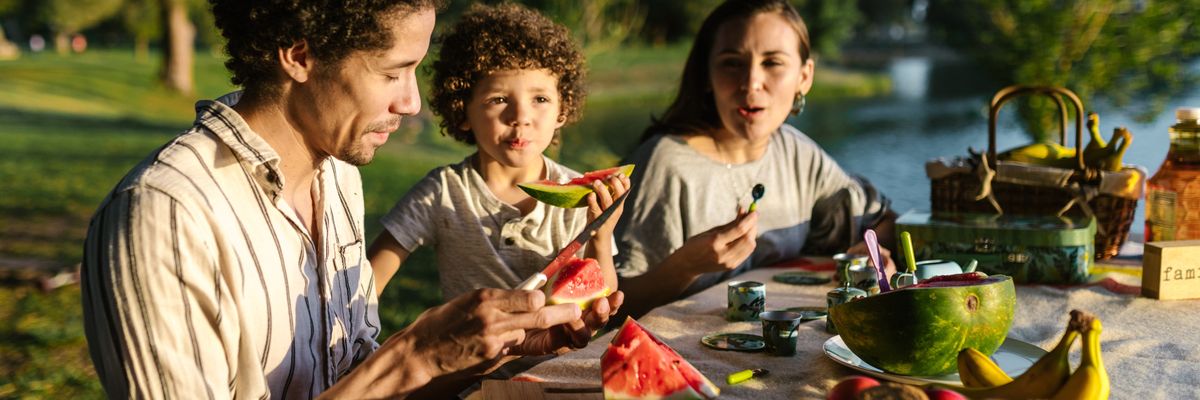 an image of a man, a child, and a woman eating watermelon at a picnic table