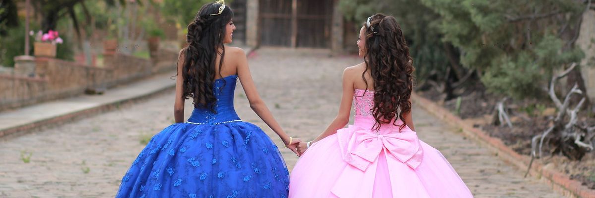 two girls in their blue and pink quinceañera dresses holding hands and walking away from the camera