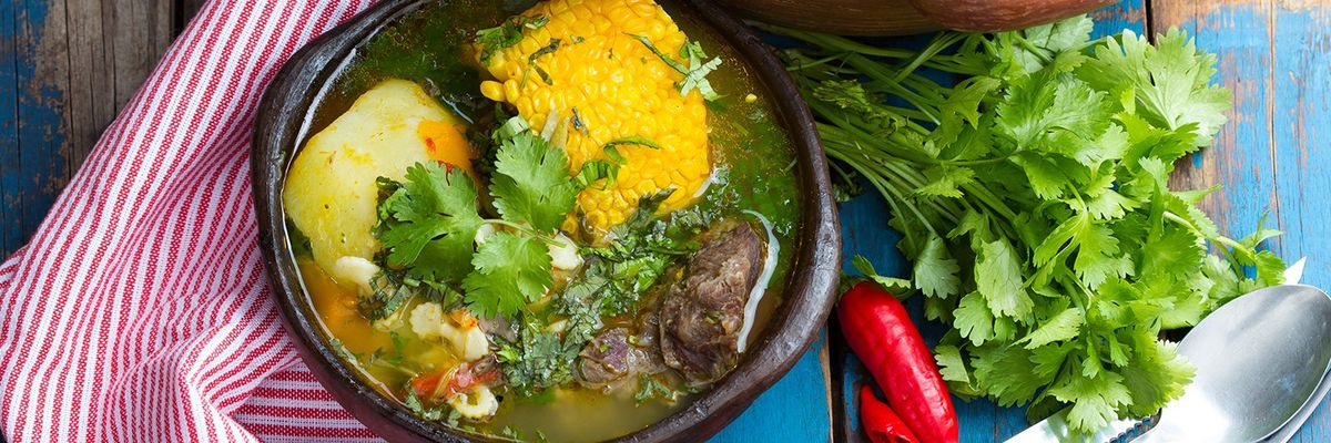 a chicken soup or "caldo" on a wooden table with cilantro and chili peppers on the side