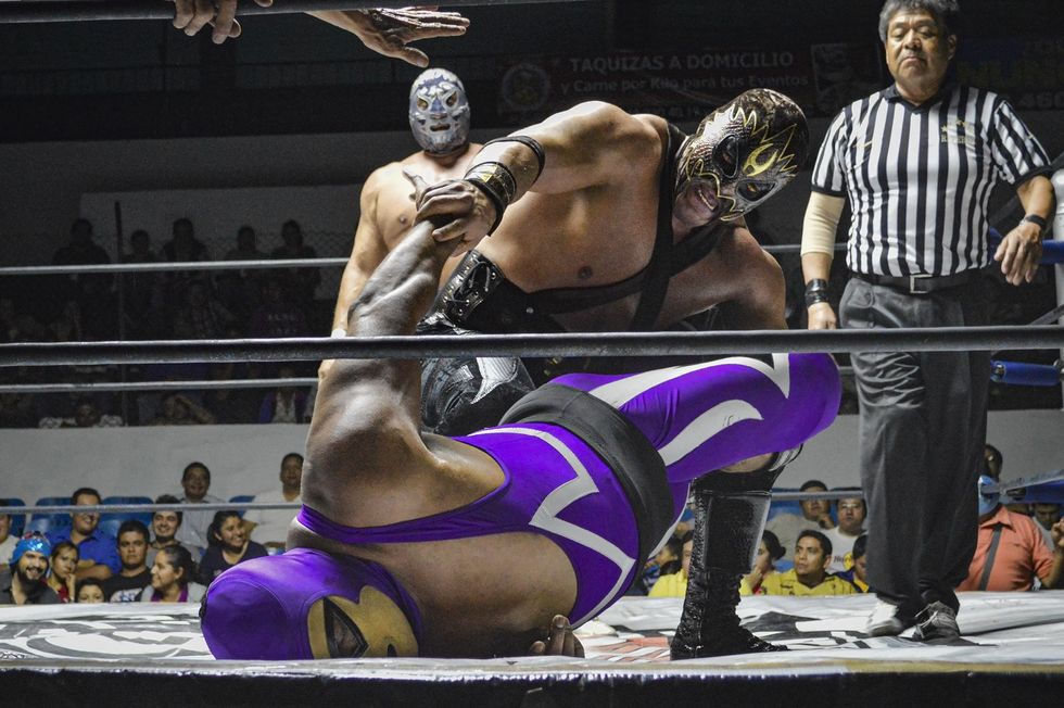 a luchador holding another man upside down in a deadlock