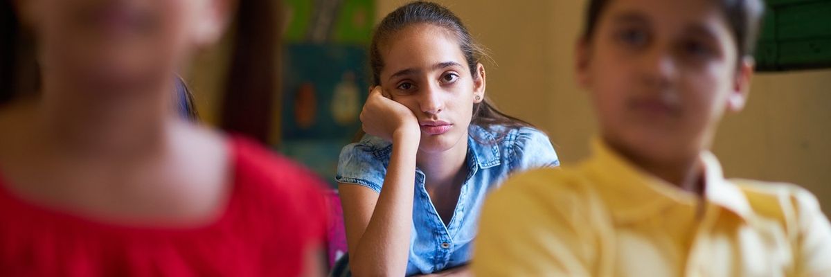 a photo of a girl in school looking bored behind two classmates