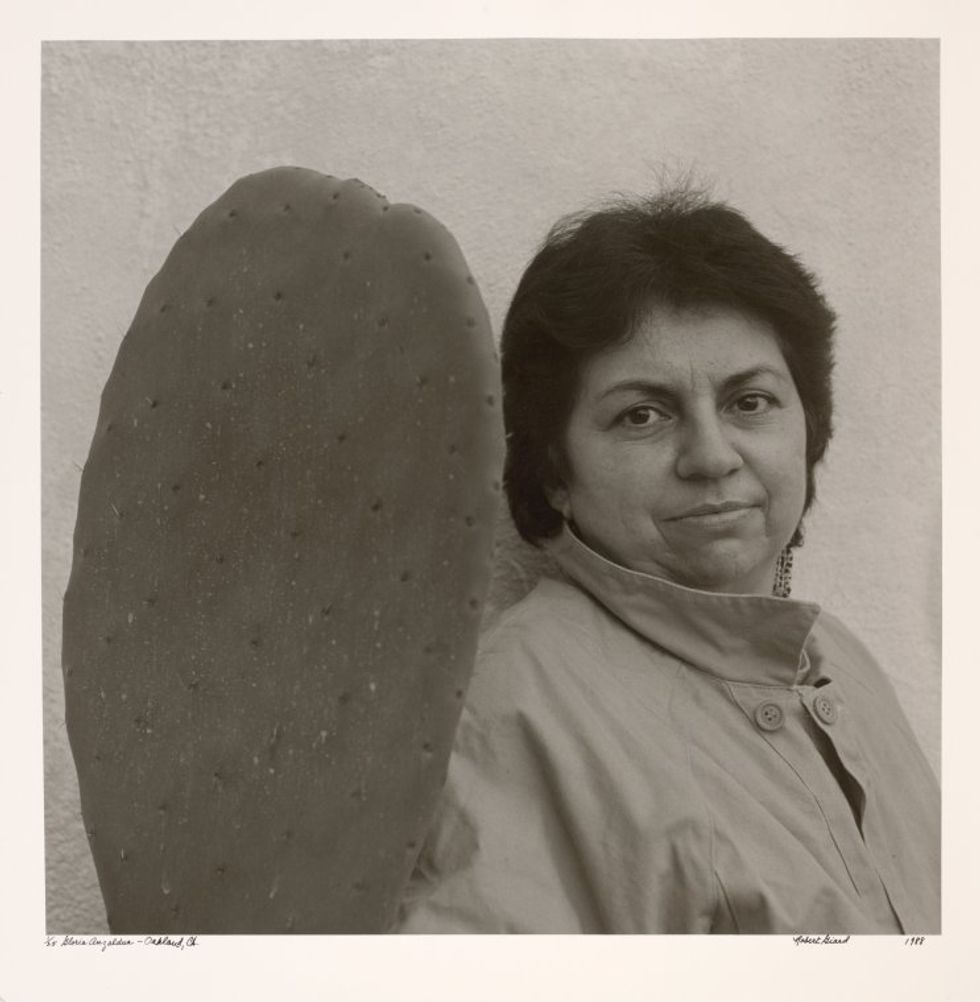 A sepia photograph of Gloria Anzald\u00faa standing next to a nopal