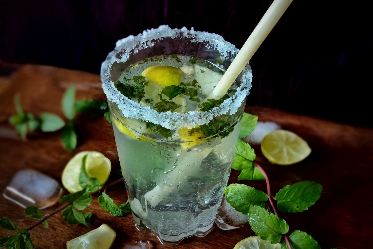 clear drinking glass with ice cubes and green leaves, a delicious mojito