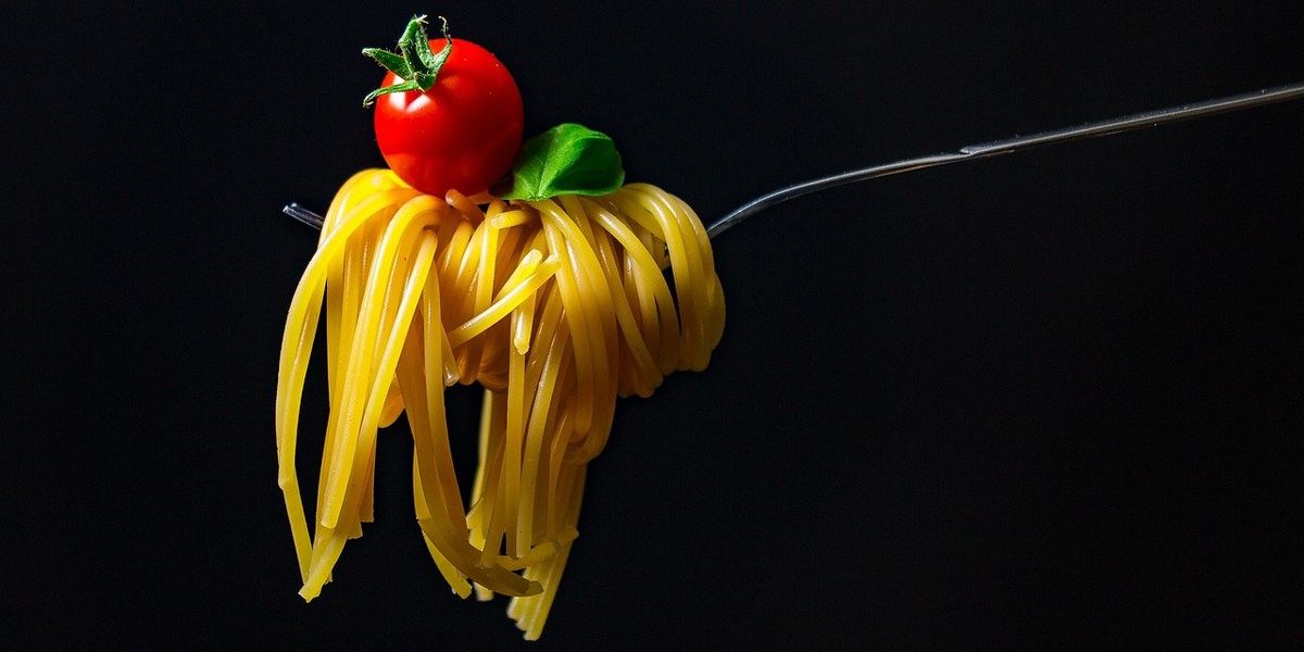 A photo of spaghetti, a tomato and a basil leaf on a fork