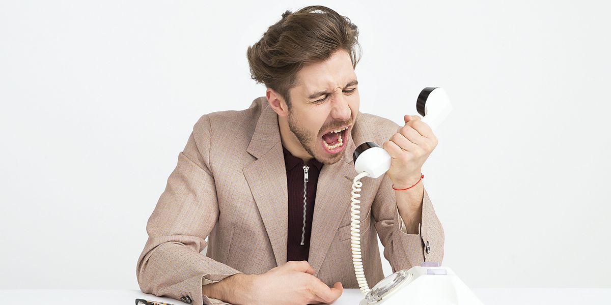man holding telephone screaming into it