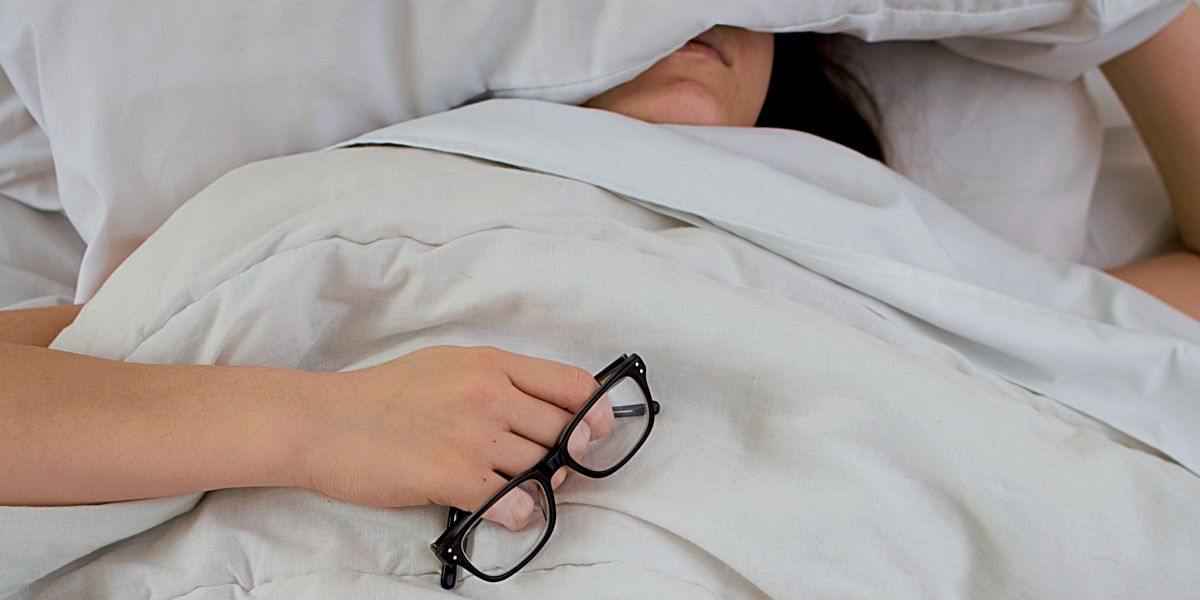 Person lying in bed with pillow covering their face