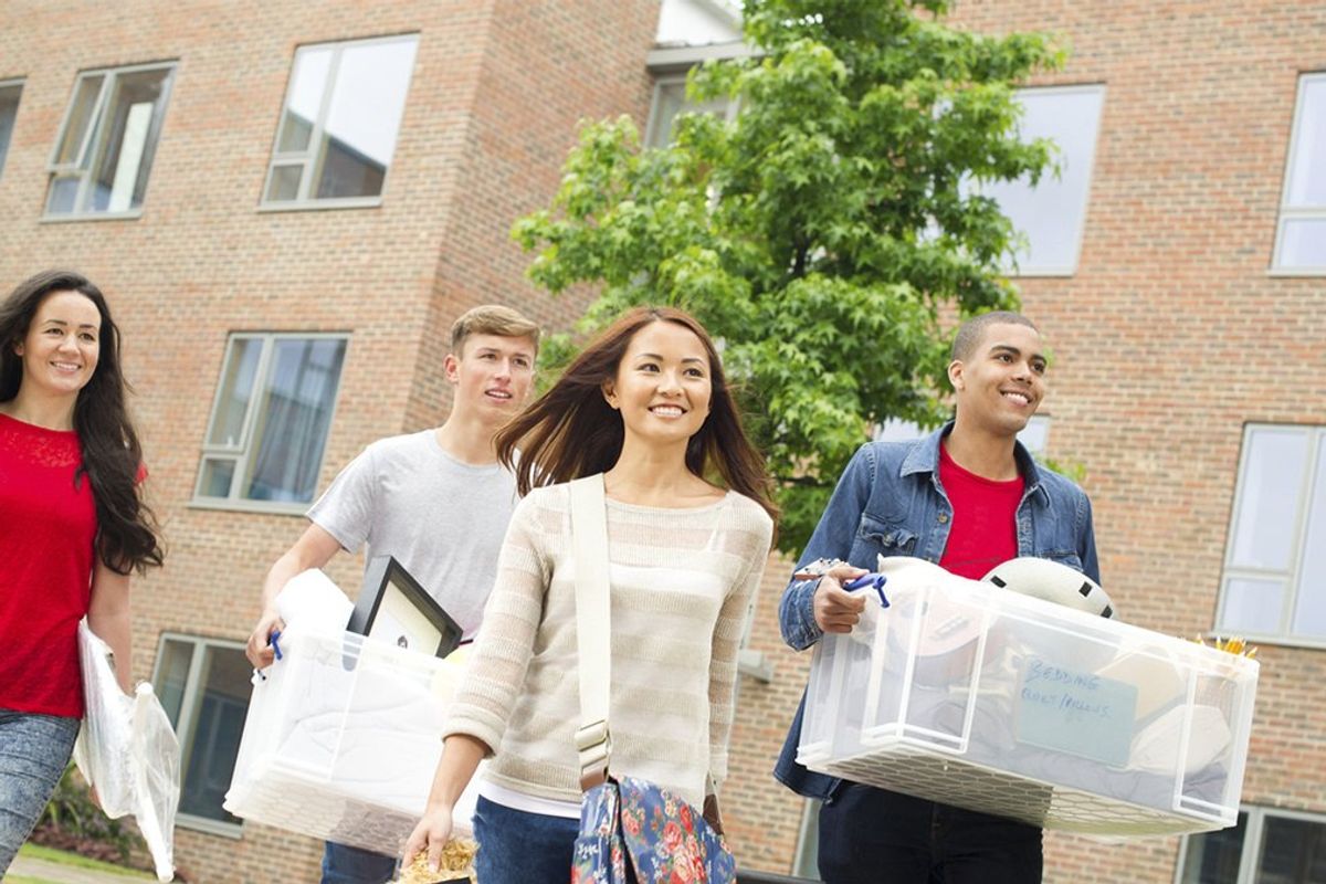 Four college students prepare to move into a dorm building with their belongings from home.