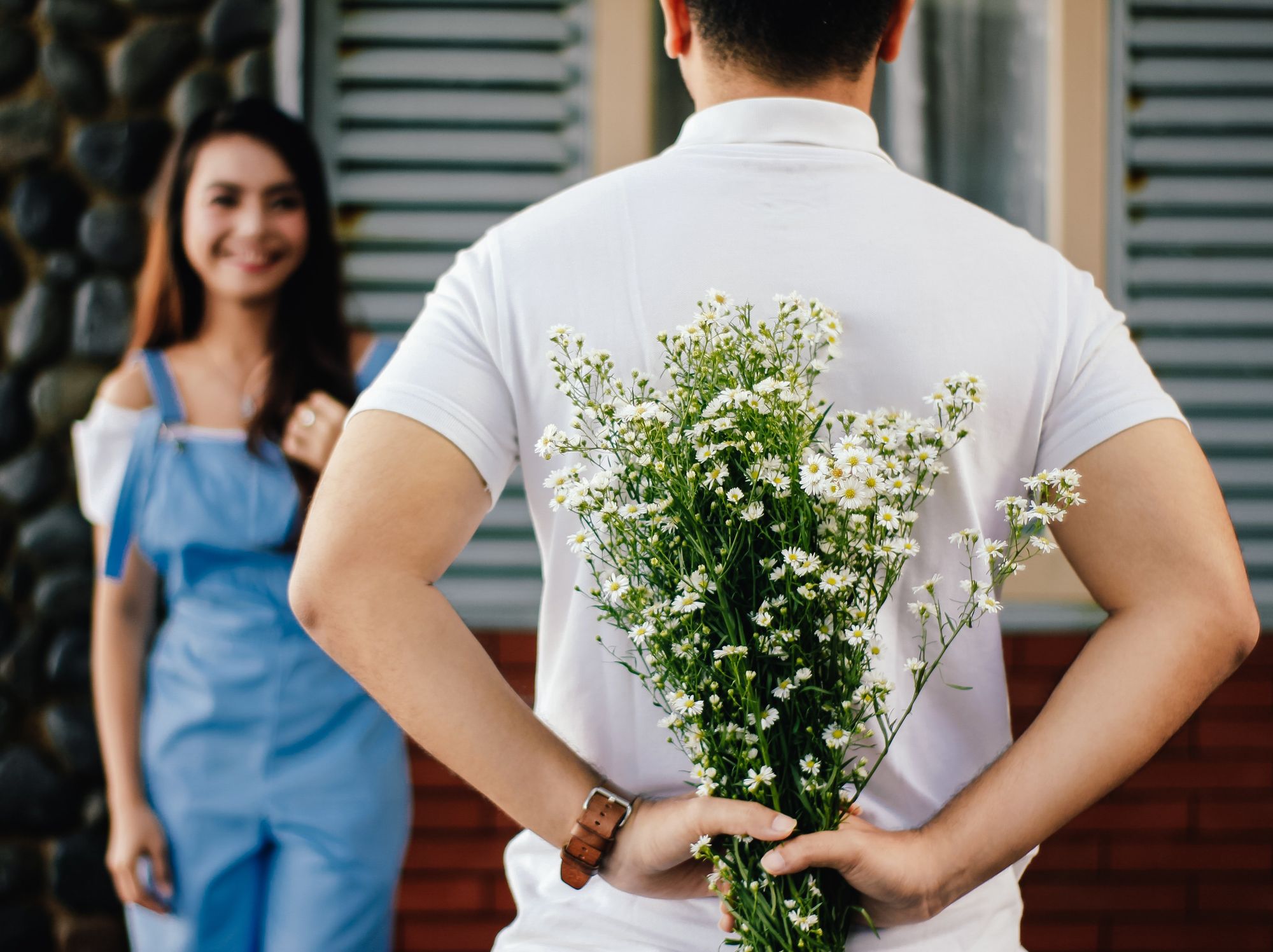 an image of a man with flowers behind his back and a woman in front of him