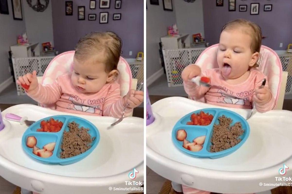 baby in a highchair eating with a spoon and fork