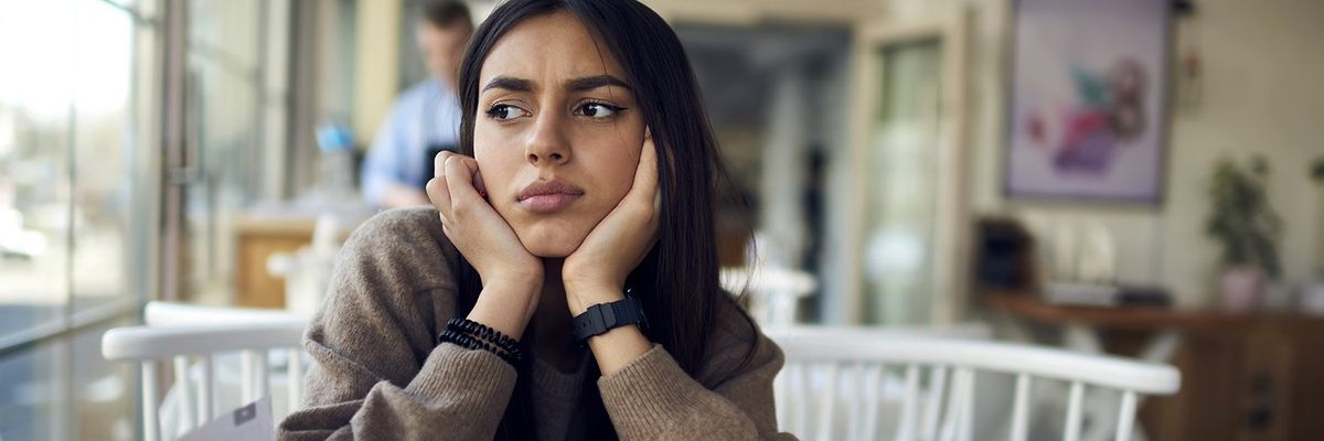 women with black hair holds her head in her hands and looks off in the distance 