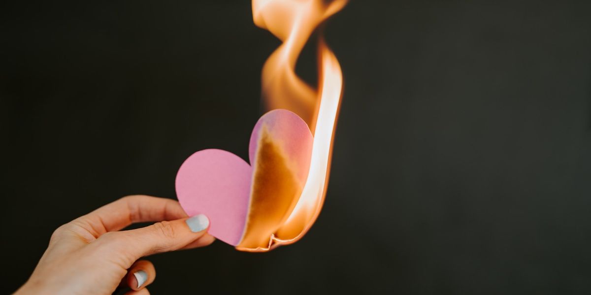 A woman's hand holds a pink paper heart that is on fire