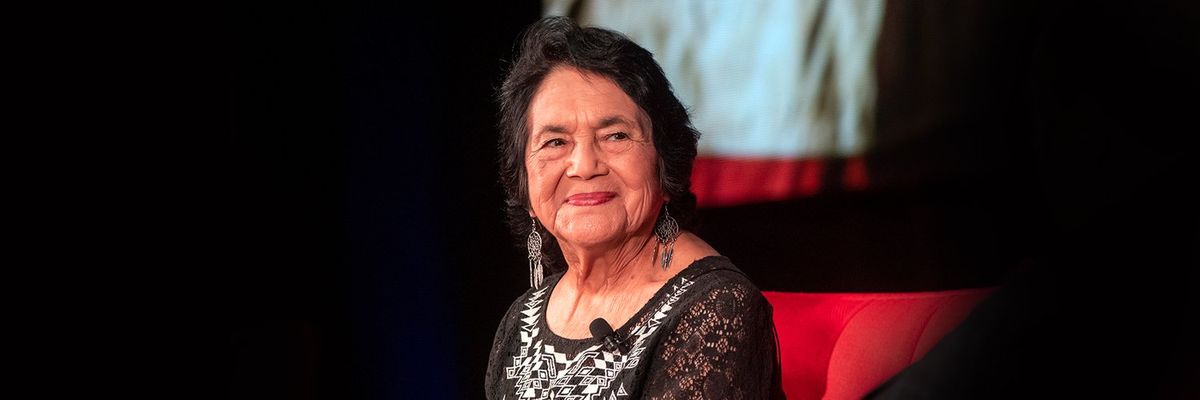 Dolores Huerta smiling sitting on a red couch 