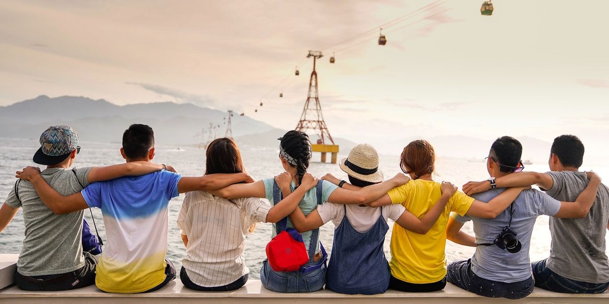 A group of friends sit with their arms around one another's shoulders while looking out into the sea