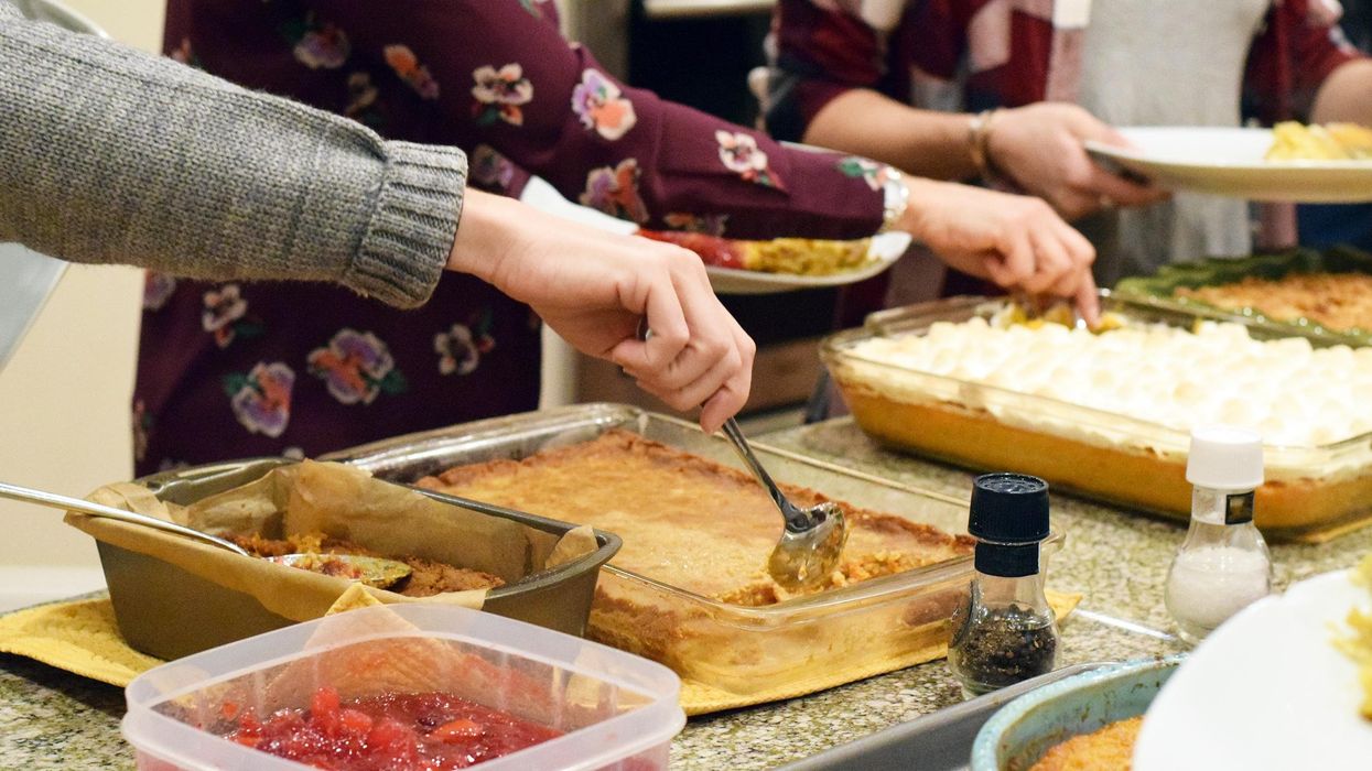 A counter is full of multiple casserole dishes, as people take their turns serving themselves from the delicious selections.