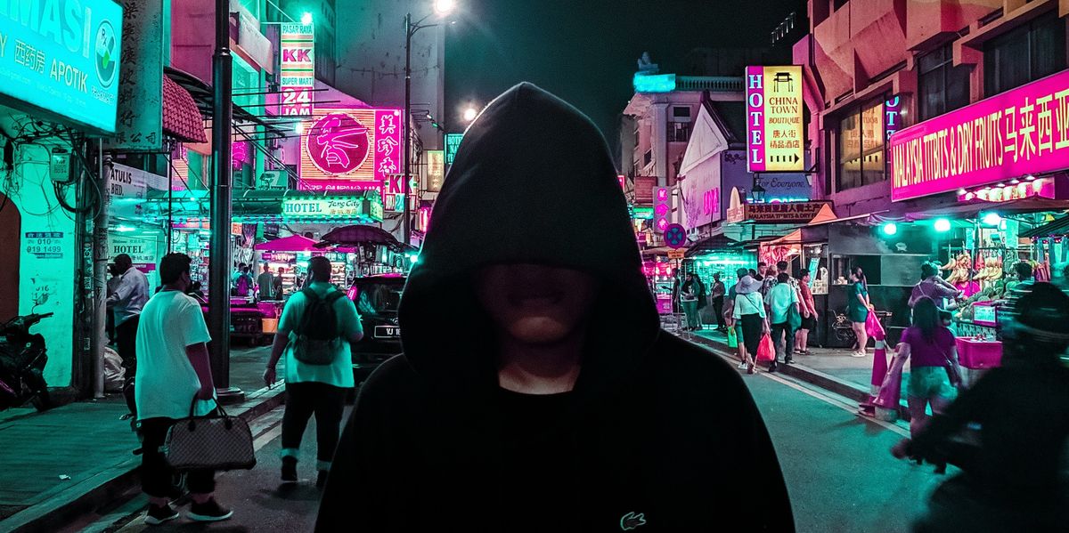 Hooded person walking down busy street at night