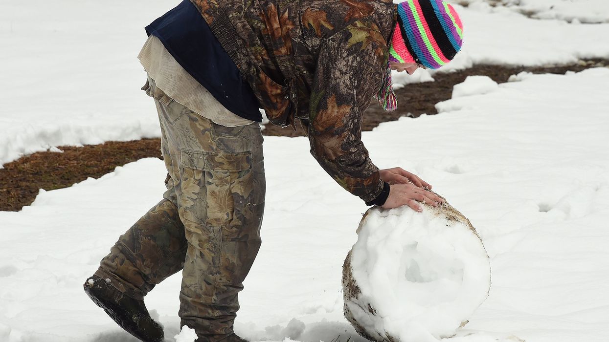 A man in a toboggan hat plays in the snow.