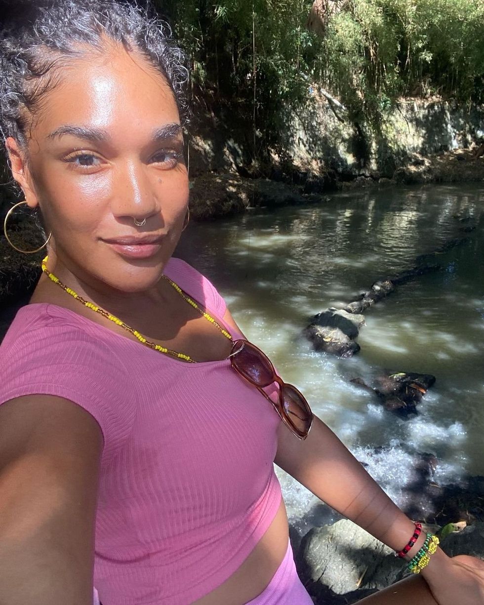 A selfie of a woman in a pink shirt and hoop earrings with a river behind her