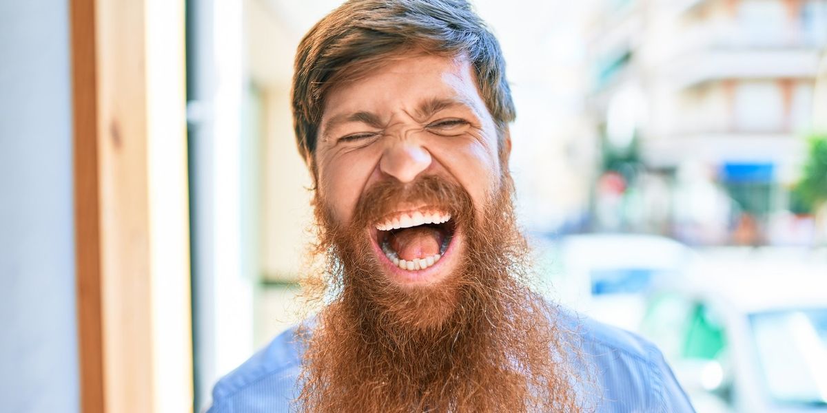 A man with a long, scraggily red beard laughs with his mouth wide open